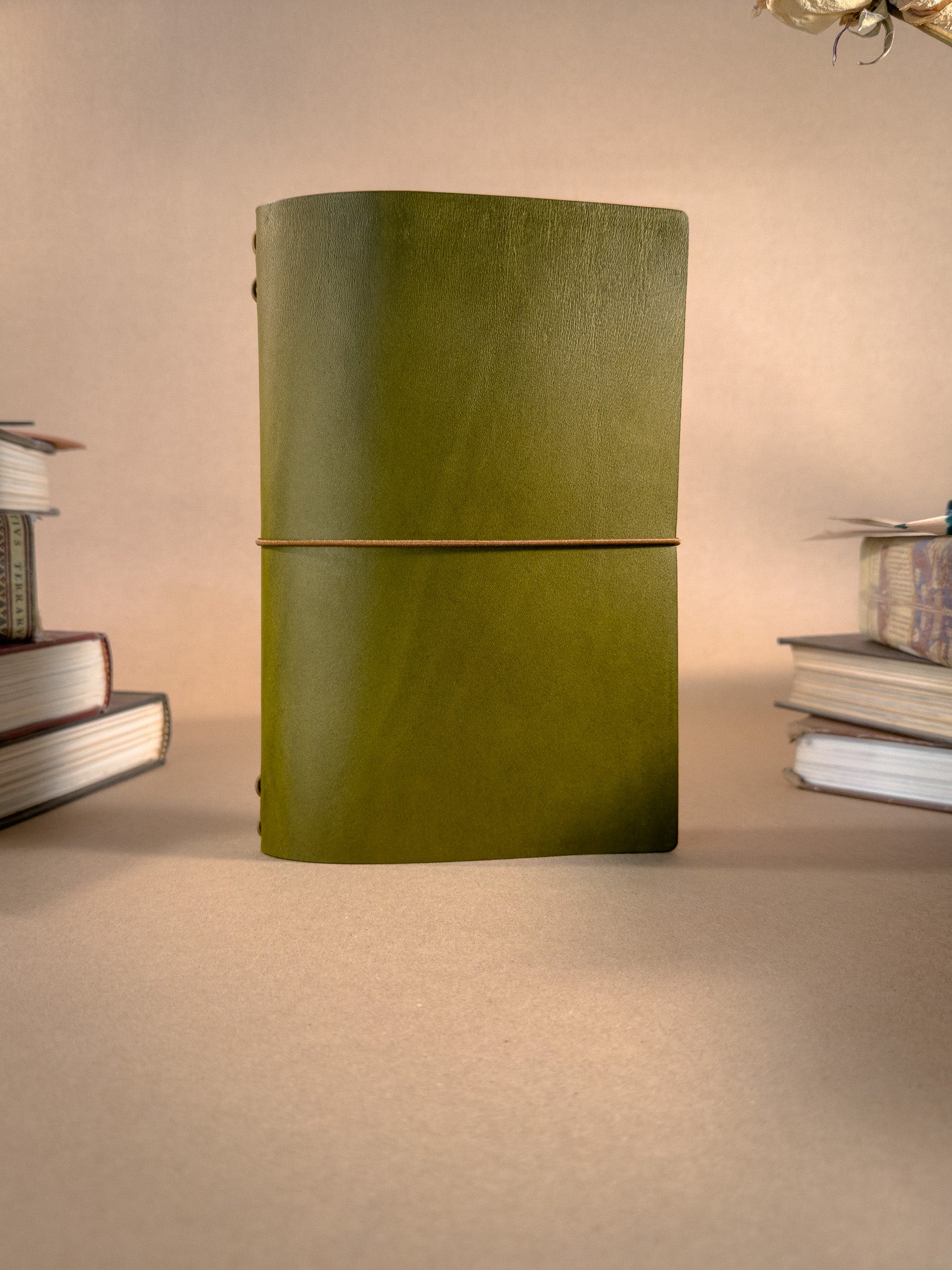 Green leather notebook on a beige surface with books in the background