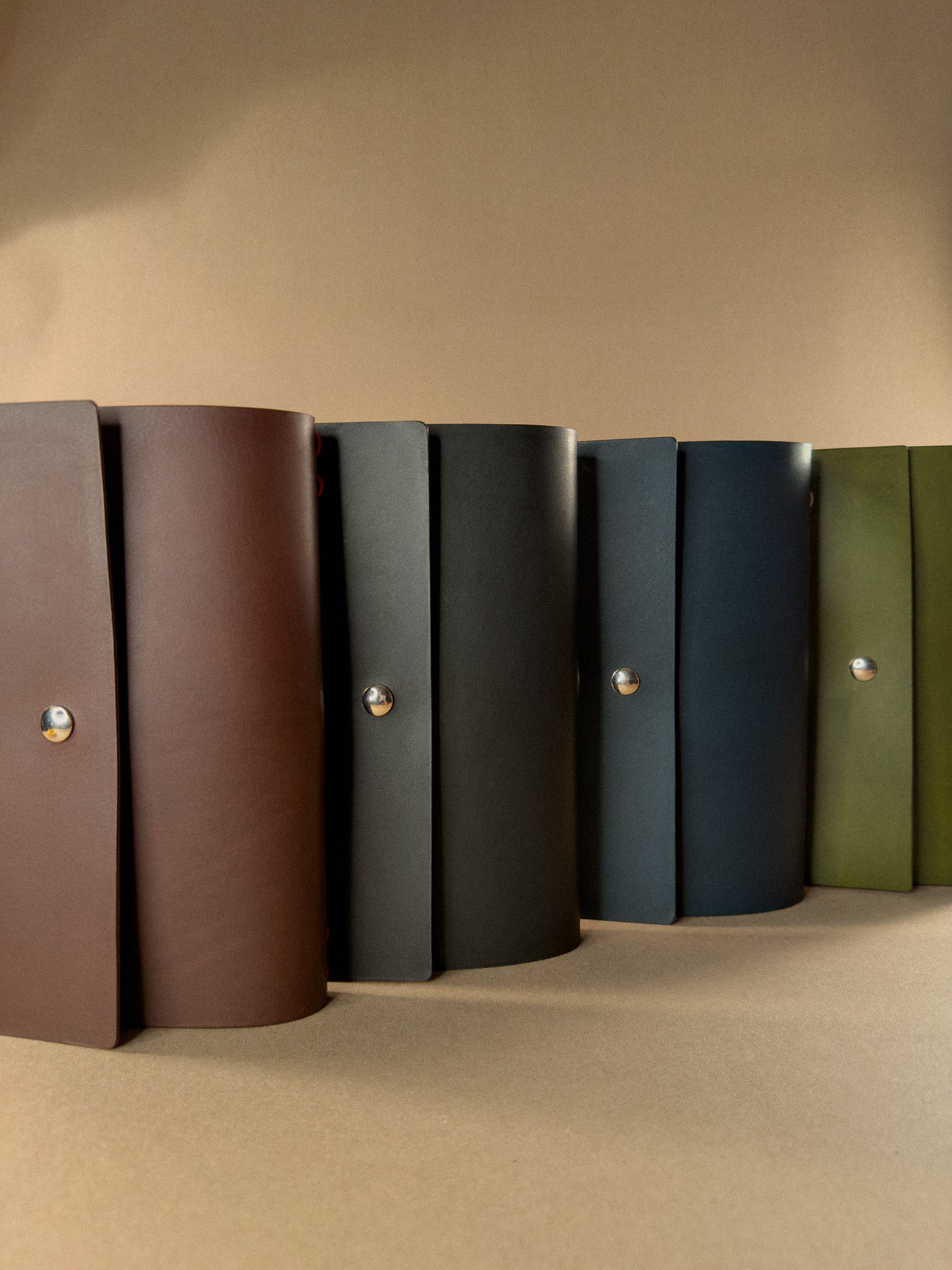 Row of leather journals in various colors on a beige surface