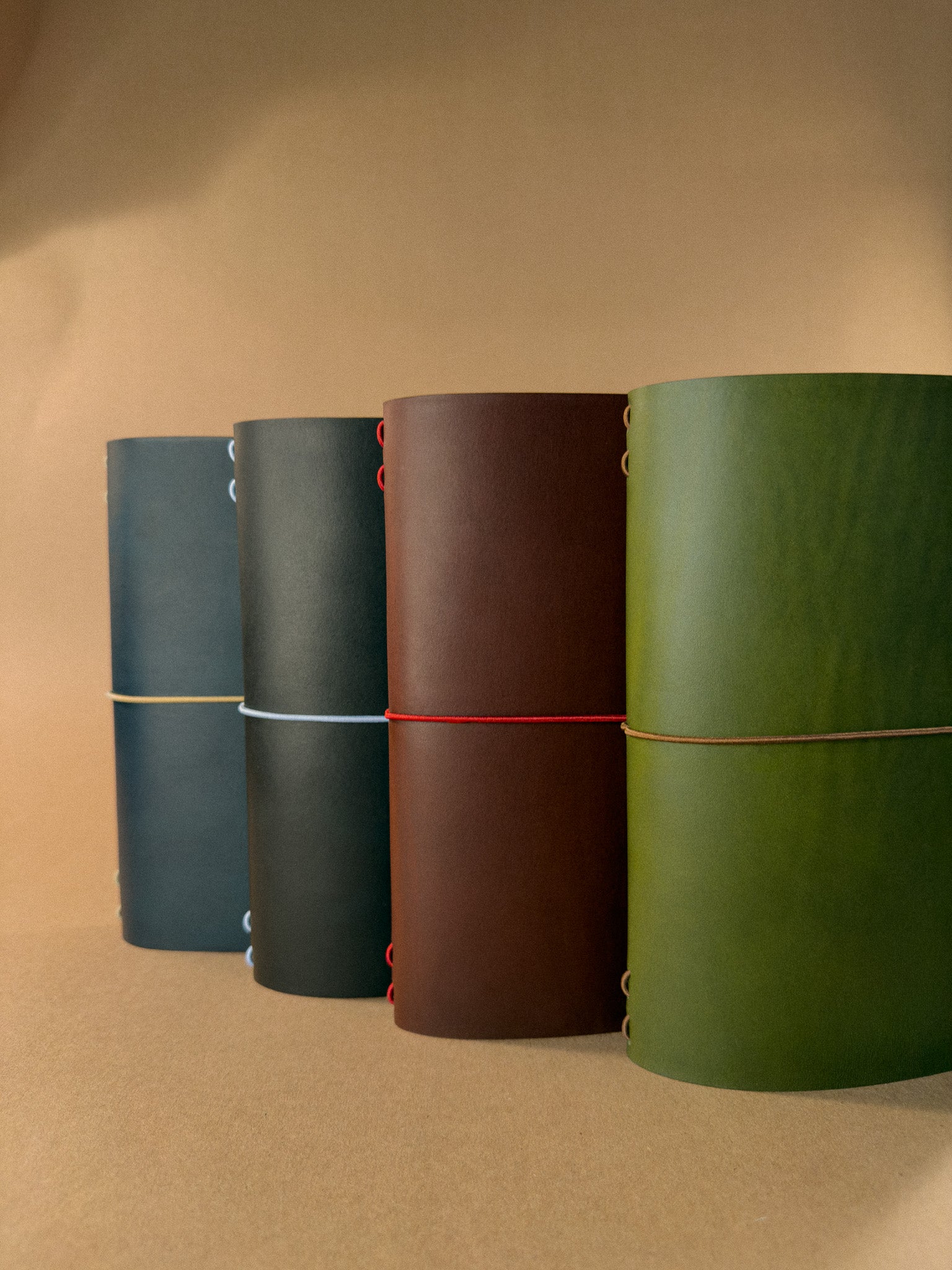 Four leather journals in different colors on a beige background