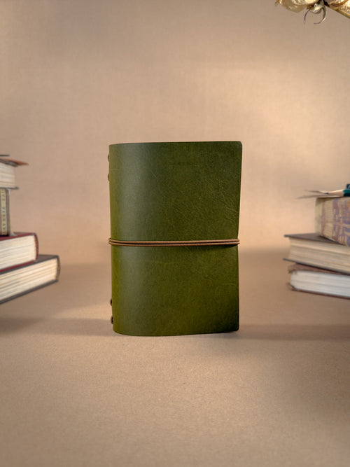 A Green pocket sized leather Journal on a beige backround